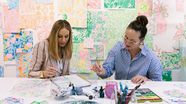 Two women sitting at a table surrounded by colorful printed artwork